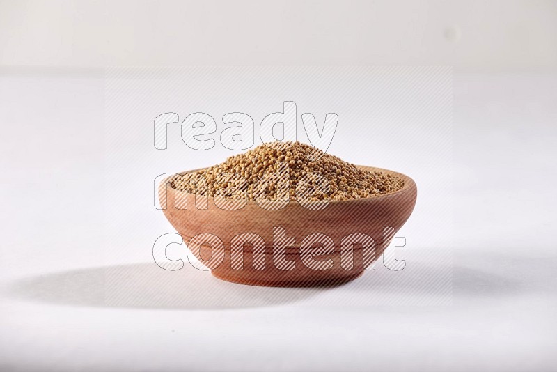 A wooden bowl full of mustard seeds on a white flooring