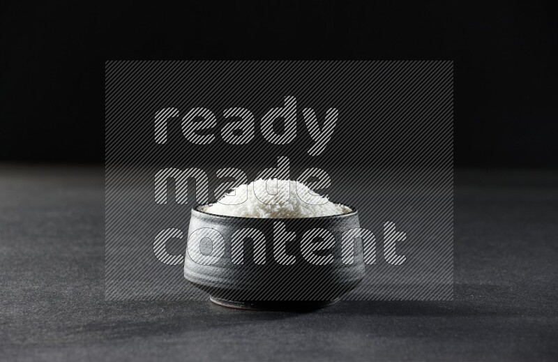 A black pottery bowl full of desiccated coconut on a black background in different angles