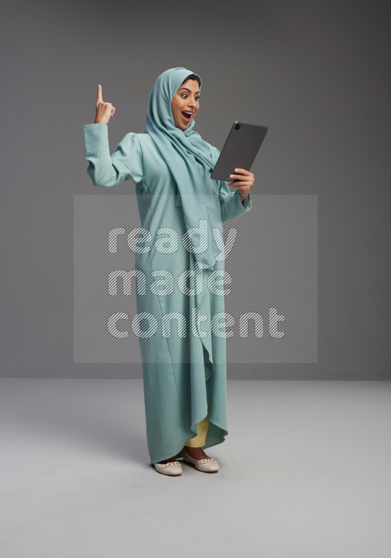 Saudi Woman wearing Abaya standing working on tablet on Gray background