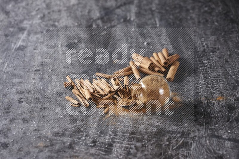 قرفة في وعاء زجاجي مقلوب مع ملعقة معدنية و أعواد القرفة علي خلفية سوداء