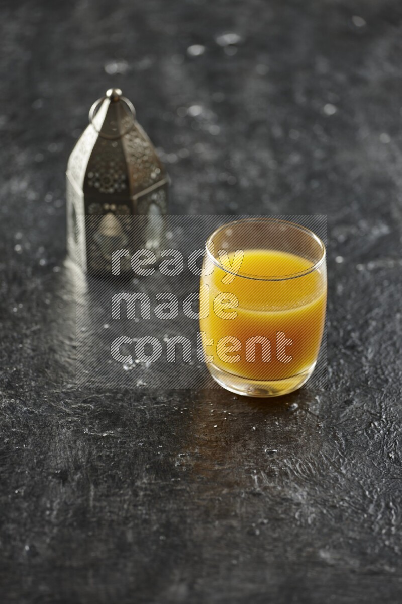 A silver lantern with different drinks, dates, nuts, prayer beads and quran on textured black background