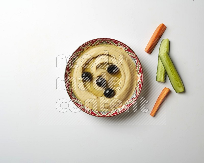 Hummus in a red plate with patterns garnished with black olives on a white background