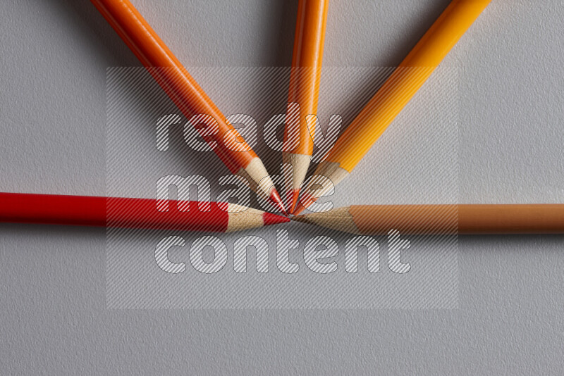 An arrangement of colored pencils in shades of orange and red on grey background