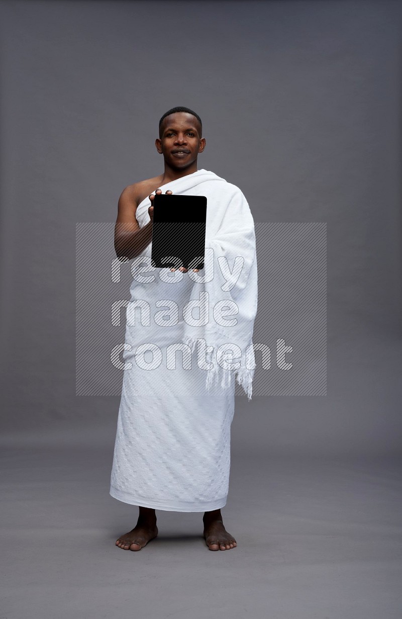 A man wearing Ehram Standing showing tablet to camera on gray background