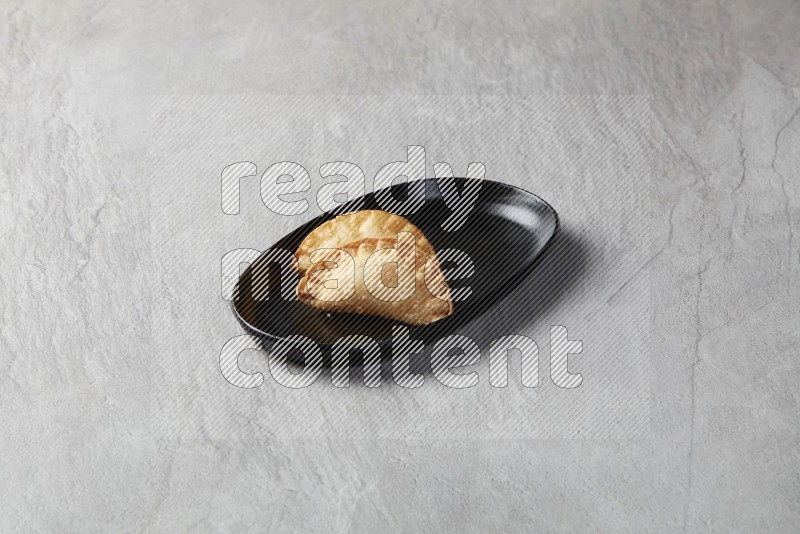 Two fried sambosas in an oval shaped black plate on a gray background