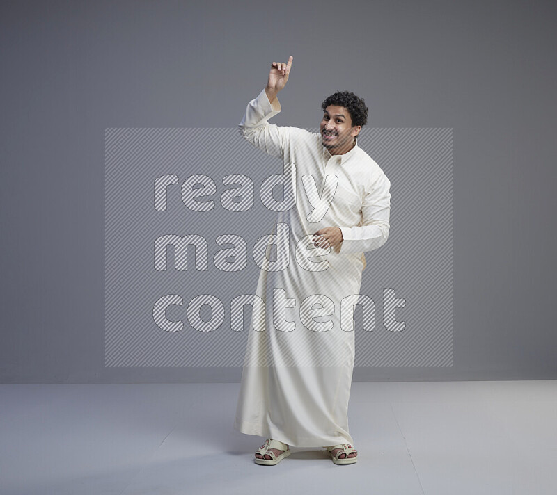 A Saudi man standing wearing thob interacting with the camera on gray background