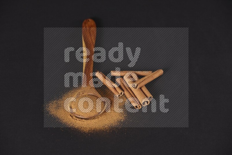 Cinnamon powder in a wooden ladle spoon with cinnamon sticks on black background