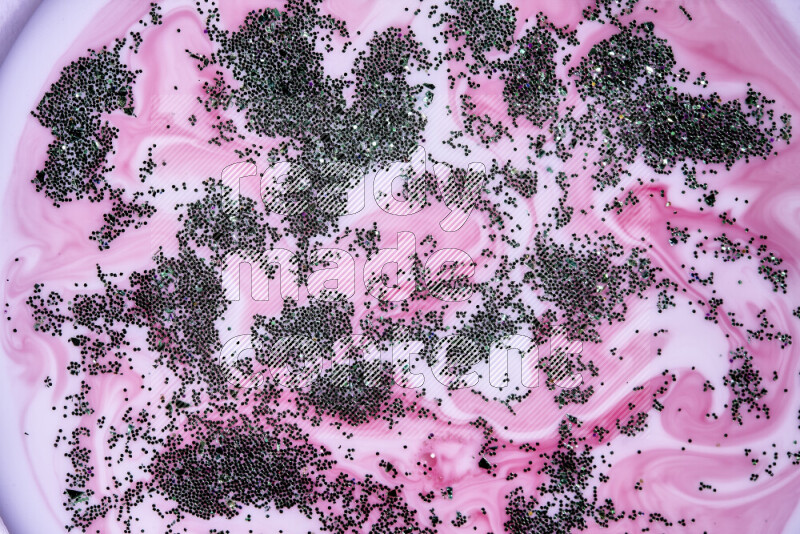 A close-up of sparkling green glitter scattered on swirling pink background