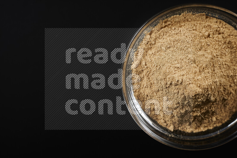 A glass bowl full of ground ginger powder on black background