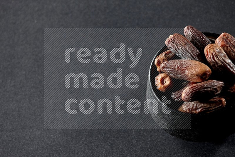 A black ceramic bowl full of dried dates on a black background in different angles