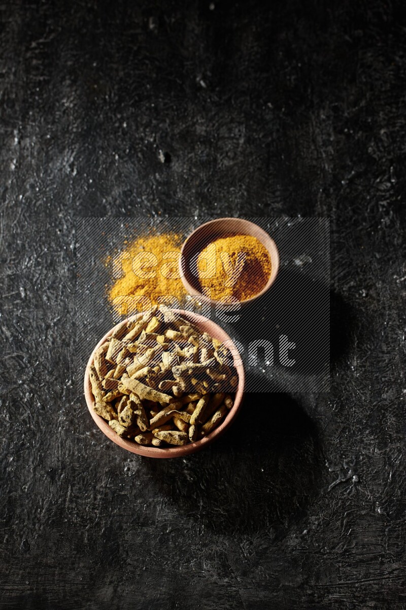 وعاءان خشبيان، أحدهما ممتلئ ببودرة الكركم والآخر بأصابع الكركم المجففة، على خلفية سوداء