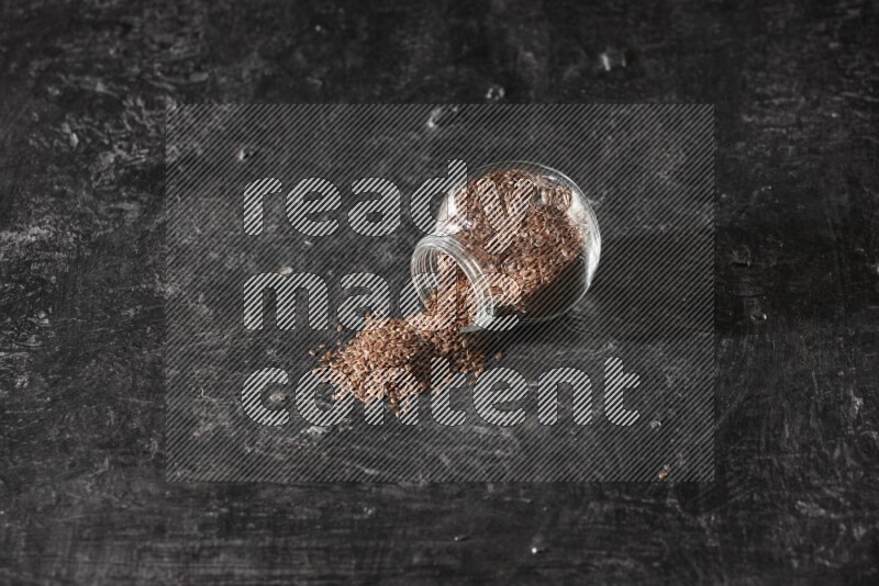 وعاء زجاجي مقلوب ممتلئ بحبوب بذر الكتان والحبوب متناثرة منه علي خلفية سوداء