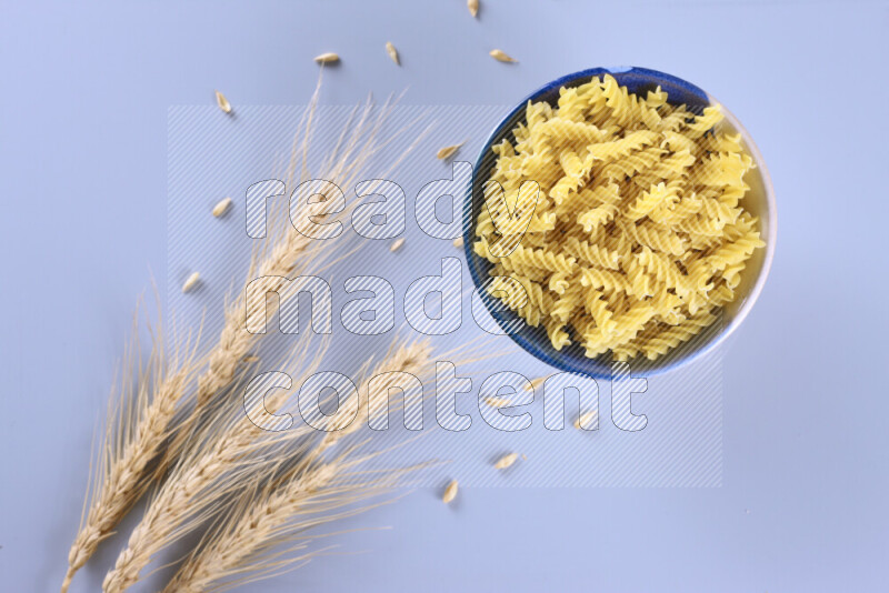 Raw pasta with wheat stalks on light blue background