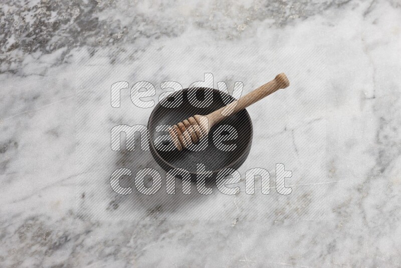 وعاء فخاري أسود مع ملعقة عسل خشبية بداخله على خلفية من الرخام الرمادي