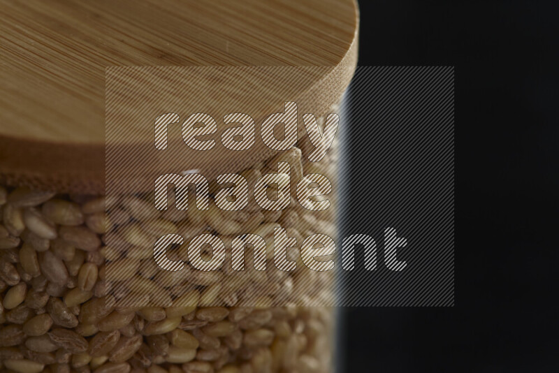 Hulled wheat in a glass jar on black background