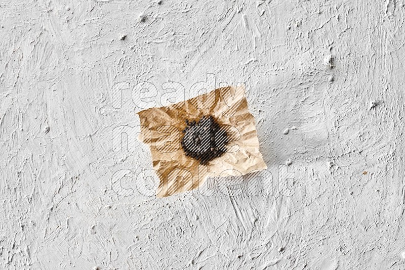 Black pepper on a crumpled paper on a textured white flooring
