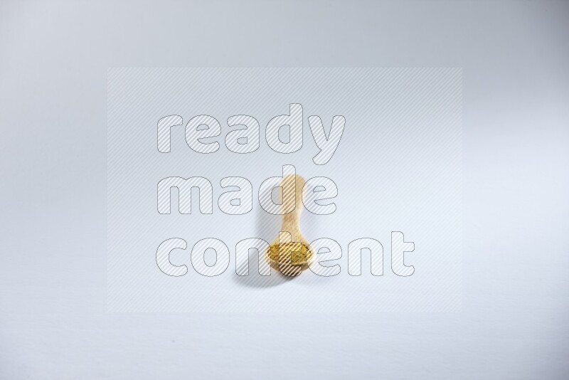 A wooden spoon full of turmeric powder on white flooring