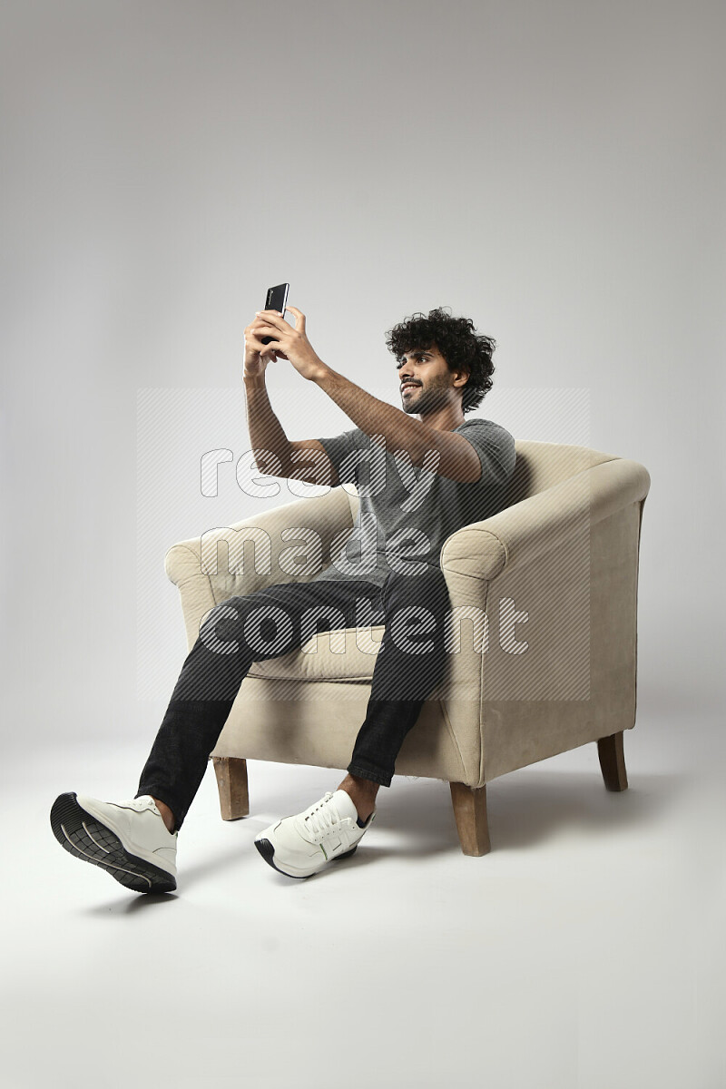رجل يرتدي ملابس كاجوال يجلس علي كرسي و يلتقط صورة شخصية علي خلفية بيضاء