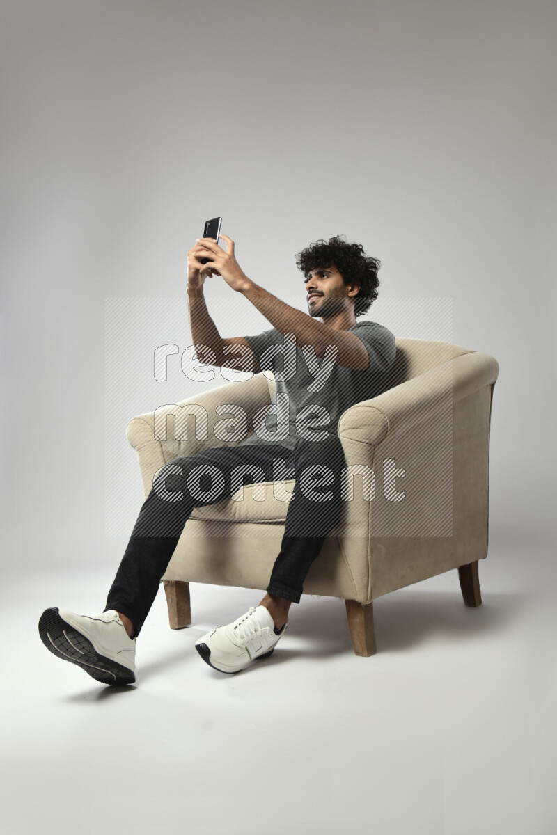 A man wearing casual sitting on a chair taking a selfie on white background