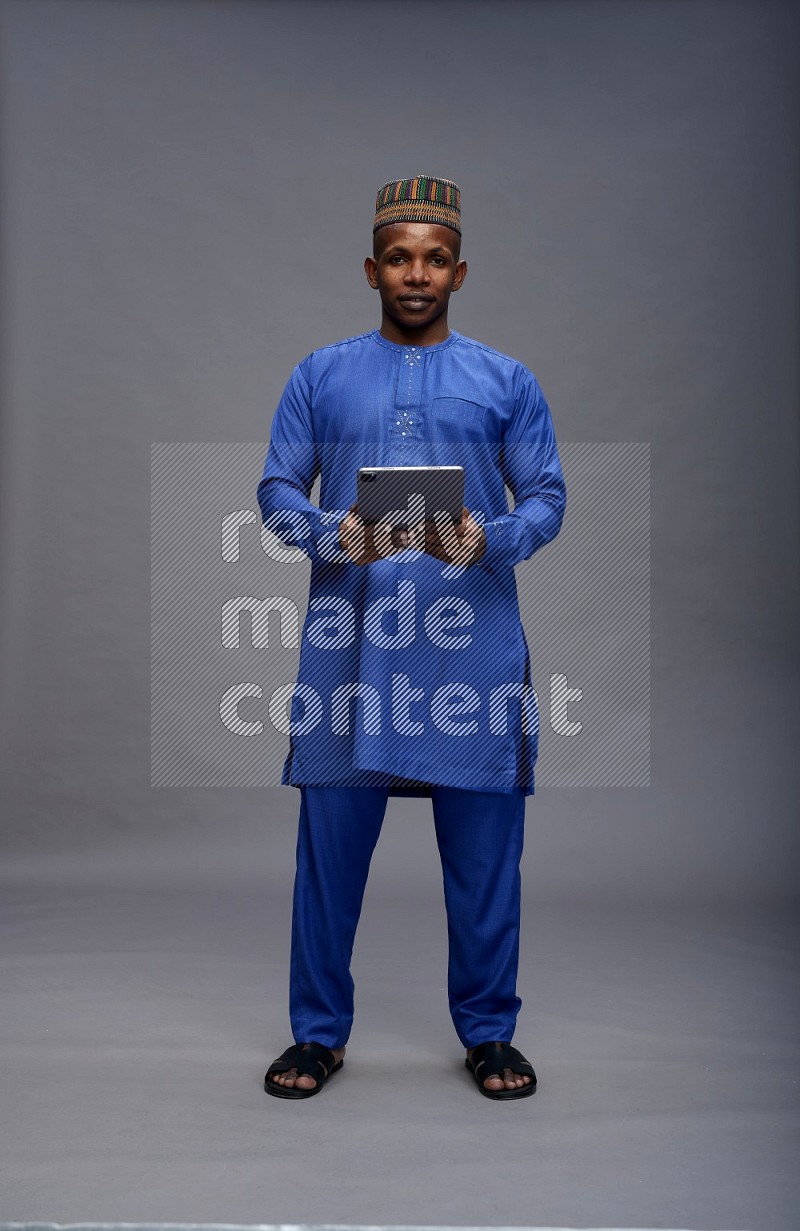 Man wearing Nigerian outfit standing working on tablet on gray background