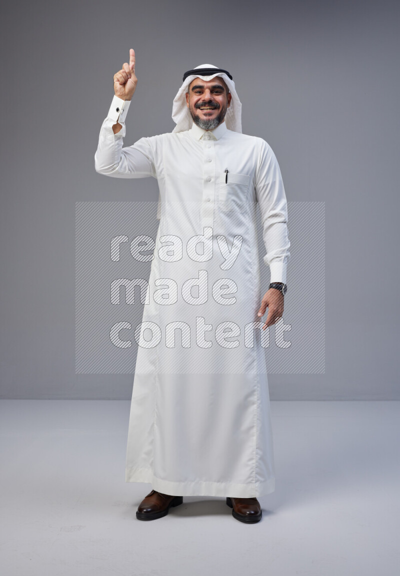 Saudi man Wearing Thob and white Shomag standing interacting with the camera on Gray background