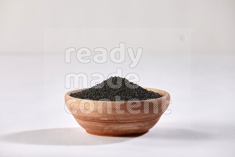 A wooden bowl full of black seeds on a white flooring