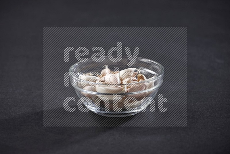 A glass bowl full of garlic cloves on a black flooring in different angles