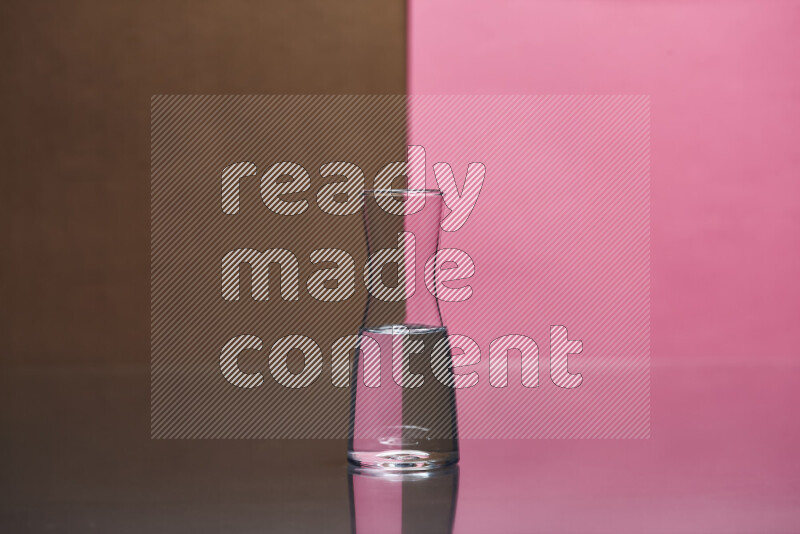 The image features a clear glassware filled with water, set against brown and pink background