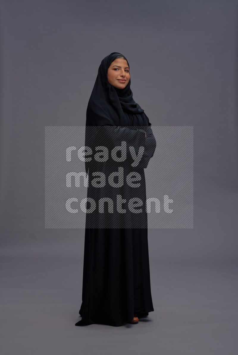 Saudi woman wearing Abaya standing with crossed arms on gray background