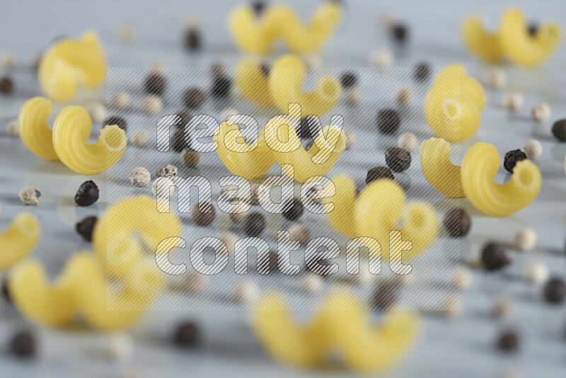 Raw pasta with different ingredients such as cherry tomatoes, garlic, onions, red chilis, black pepper, white pepper, bay laurel leaves, rosemary, cardamom and mushrooms on light blue background