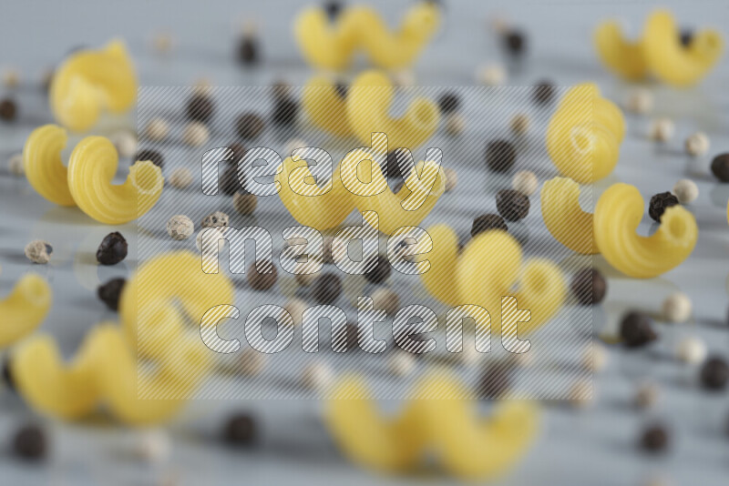Raw pasta with different ingredients such as cherry tomatoes, garlic, onions, red chilis, black pepper, white pepper, bay laurel leaves, rosemary, cardamom and mushrooms on light blue background