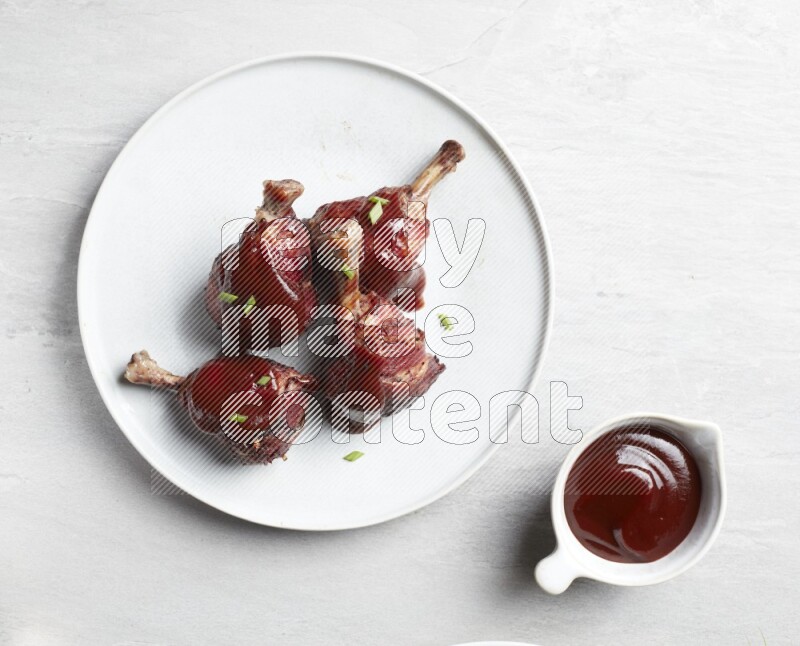 drumstick wrapped in bacon on round white ceramic plate on grey textured countertop