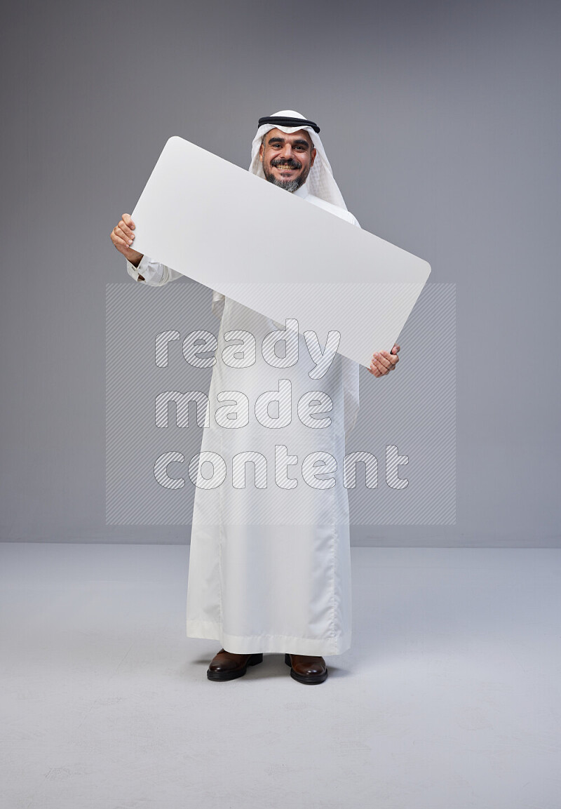 Saudi man Wearing Thob and white Shomag standing holding board on Gray background