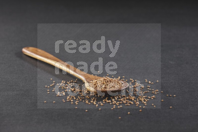 A wooden spoon full of mustard seeds on a black flooring