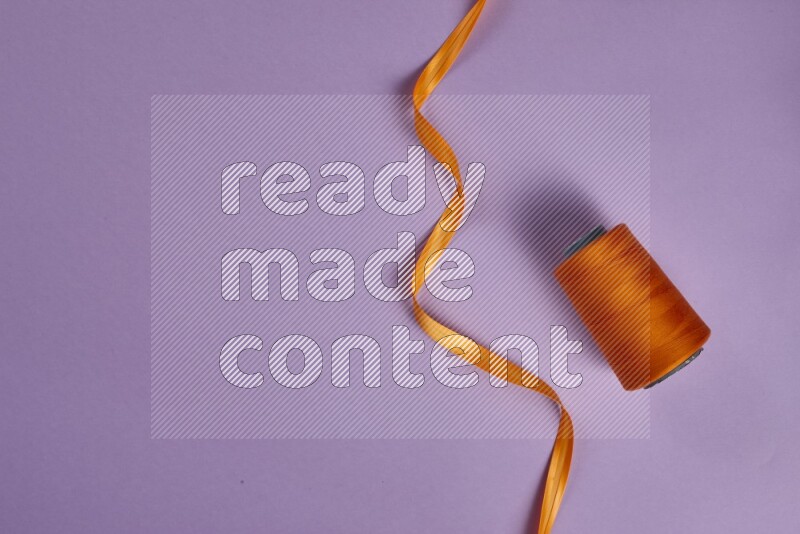 An orange collection of sewing and tailoring tools arranged on a purple background