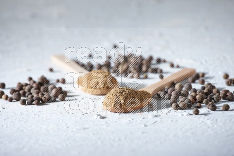 Wooden spoons full of allspice powder and allspice whole balls spreaded on a textured white flooring