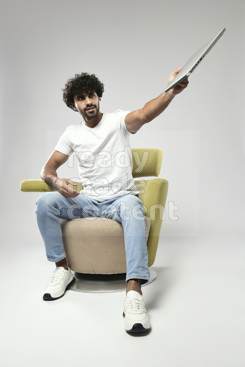 A man wearing casual sitting on a chair holding a laptop on white background