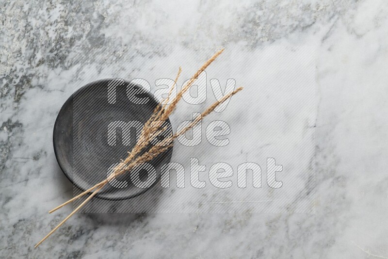 Wheat stalks on black pottery plate on grey marble background
