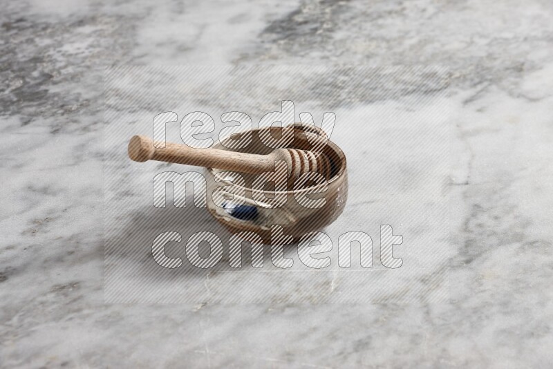 Multicolored pottery bowl with wooden honey dipper in it on grey marble background