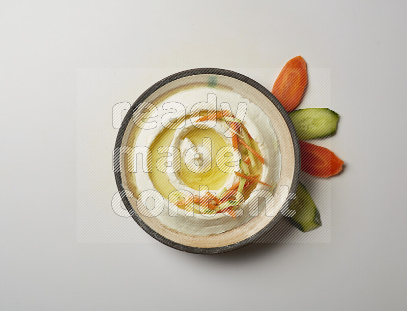 Lebnah garnished with sliced carrots &cucumber in a pottery plate on a white background