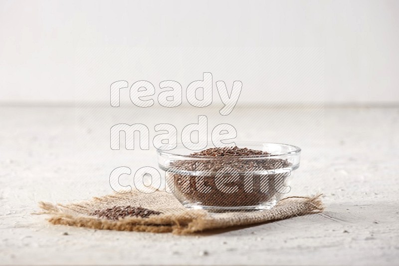 وعاء زجاجي ممتلئ بحبوب بذر الكتان مع بعض الحبوب علي قطعة من القماش علي خلفية بيضاء