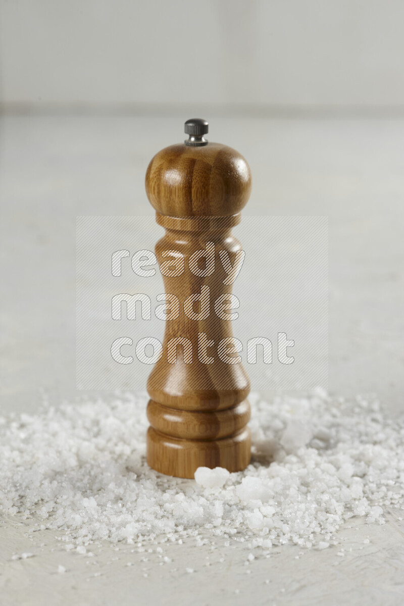 A wooden grinder standing upright and surrounded by coarse white seaa salt on white background