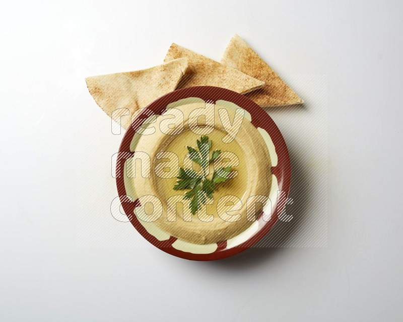 Hummus in a traditional plate garnished with parsley on a white background