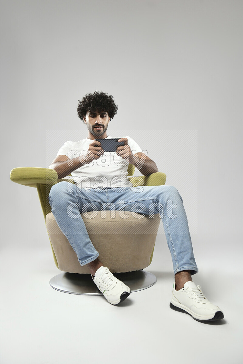 A man wearing casual sitting on a chair gaming on the phone on white background