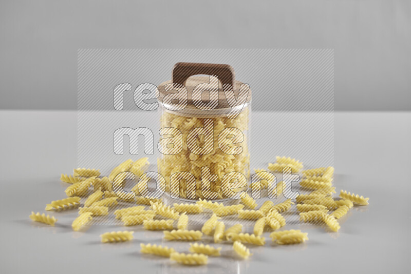 Raw pasta in a glass jar on light grey background