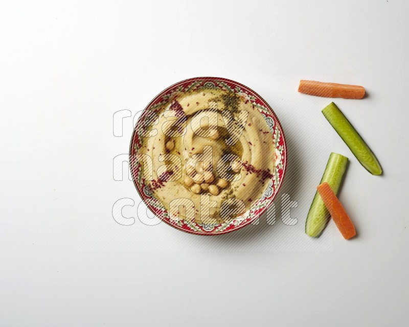 Hummus in a red plate with patterns garnished with zaatar & sumak on a white background