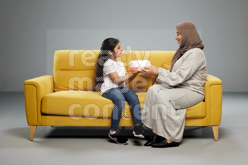 A girl sitting giving a cake to her mother on gray background