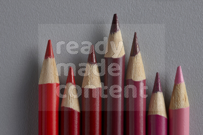 A collection of colored pencils arranged showcasing a gradient of pink and red hues on grey background