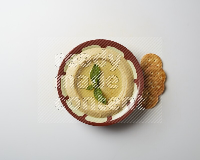 Hummus in a traditional plate garnished with mint on a white background