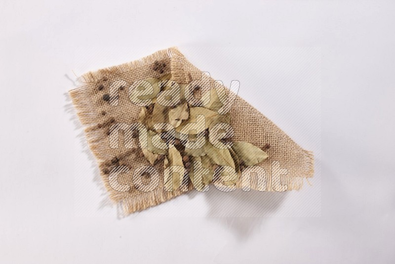 Dried bay leaves and allspice berries on a piece of burlap on white flooring in different angles